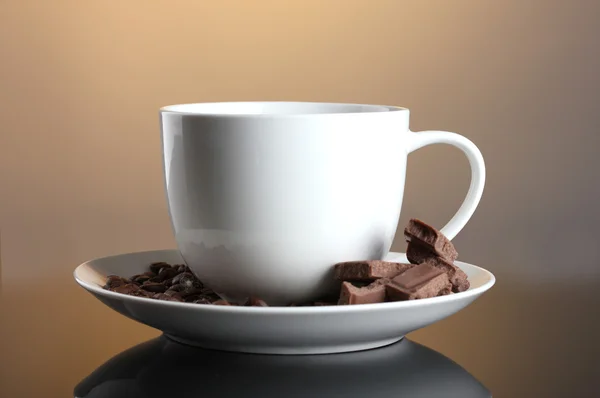 Kopje koffie, bonen en chocolade op bruine achtergrond — Stockfoto