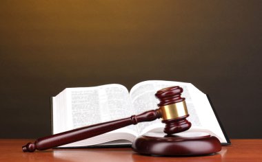 Judge's gavel and open book on wooden table on brown background clipart