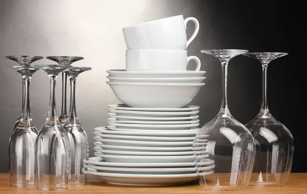 Czyste talerze, szklanki i kubki na drewnianym stole na szarym tle — Zdjęcie stockowe