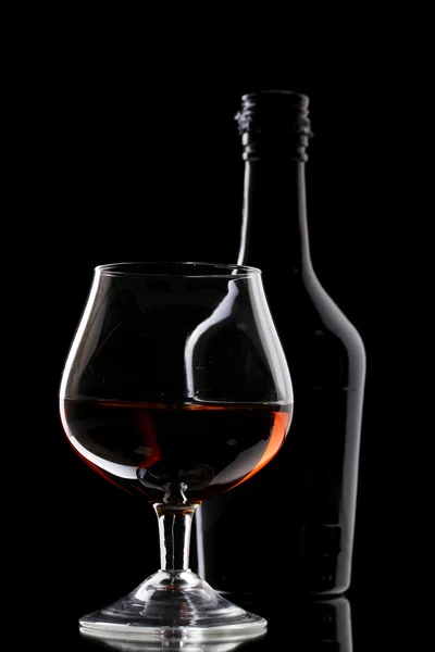 Glass of brandy and bottle on black background — Stock Photo, Image