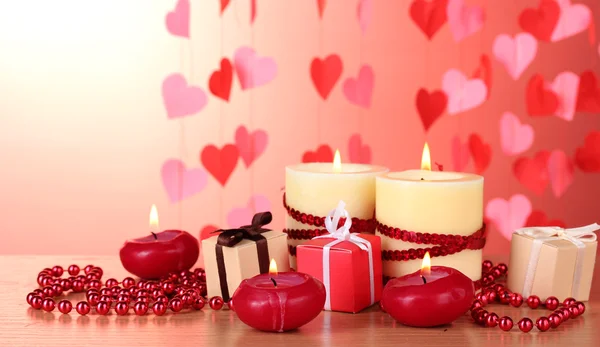 Beautiful candles with romantic decor on a wooden table on a red background — Stock Photo, Image