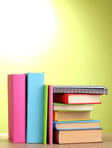 Books with stationery on wooden table on green background