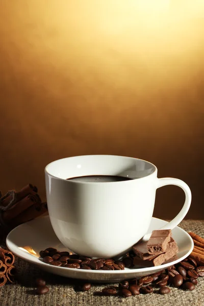 Kopje koffie en bonen, kaneelstokjes en chocolade op plundering op bruine achtergrond — Stockfoto