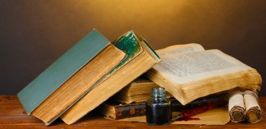 Old books, scrolls, ink pen and inkwell on wooden table on brown background clipart