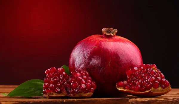 Ripe pomegranate fruit with leaves on wooden table on red background — Stock Photo, Image