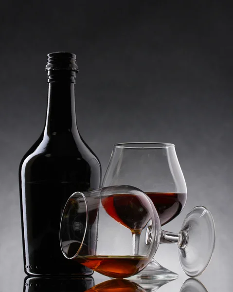 Okulary z brandy i butelka na szarym tle — Zdjęcie stockowe