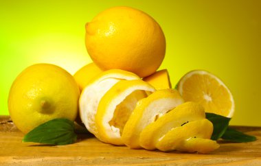 Ripe lemons with leaves on wooden table on green background clipart