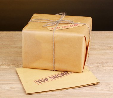 Parcel and envelope with top secret stamp on wooden table on brown background clipart