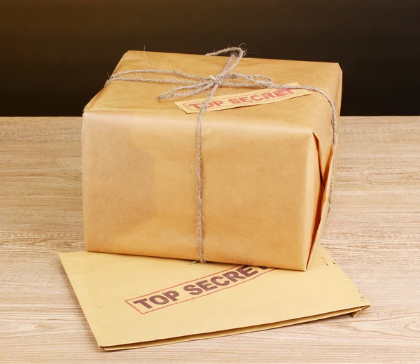 Посылка и конверт со сверхсекретной печатью на деревянном столе на коричневом фоне — стоковое фото