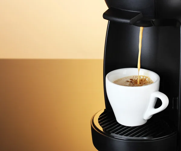 Еспресо-машина наливає каву в чашку на коричневий фон — стокове фото