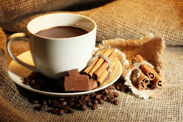 Taza de café y frijoles, palitos de canela y chocolate sobre fondo de saco —  Fotos de Stock