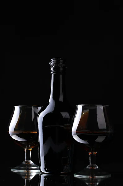 Vasos de brandy y botella sobre fondo negro — Foto de Stock