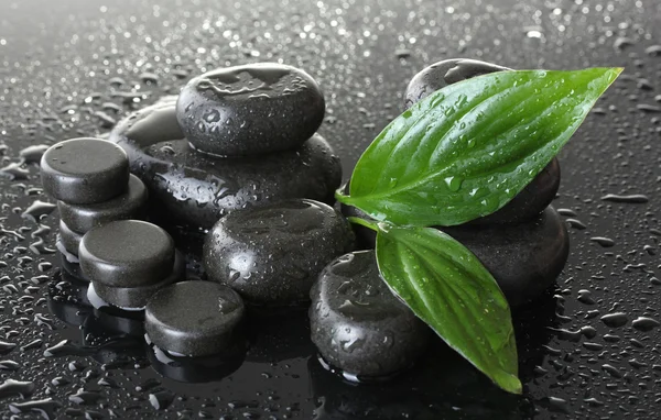 Pedras de spa com gotas e folhas verdes sobre fundo cinza — Fotografia de Stock