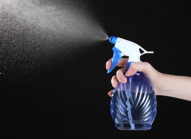 Hand holding spray bottle and spraying on black background clipart