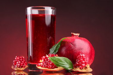 Ripe pomergranate and glass of juice on red background clipart