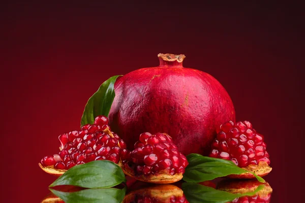 Reife Granatapfelfrucht mit Blättern auf rotem Hintergrund — Stockfoto