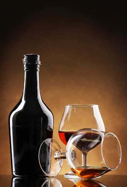 Стаканы бренди и бутылки на коричневом фоне — стоковое фото