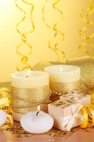 Belas velas, presentes e decoração em mesa de madeira no fundo amarelo — Fotografia de Stock