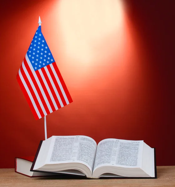 Bandeira americana no estande e livros sobre mesa de madeira no fundo vermelho — Fotografia de Stock