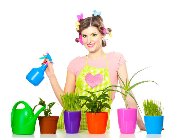 Beautiful happy young housewife sprays plants in flowerpots isolated on white