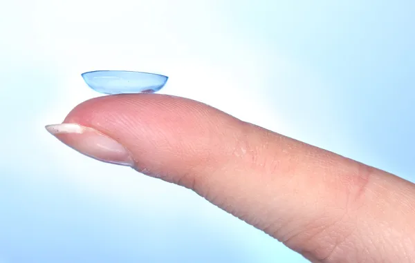 Kontaktlinse am Finger auf blauem Hintergrund — Stockfoto
