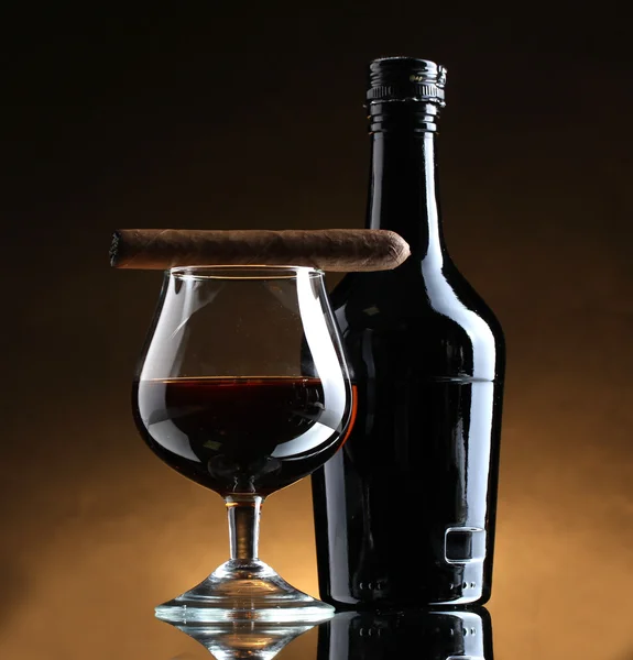Butelkę i kieliszek brandy i cygaro na brązowym tle — Zdjęcie stockowe
