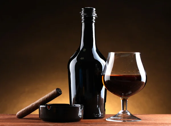 Μπουκάλι και ποτήρι κονιάκ και πούρο στο ξύλινο τραπέζι για καφέ φόντο — Φωτογραφία Αρχείου