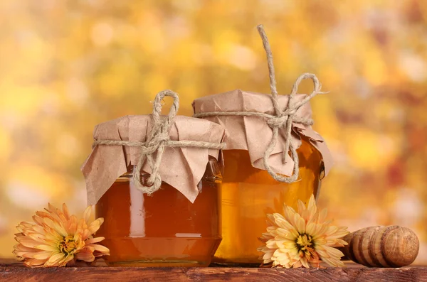 Two jars of honey and wooden drizzler on table on yellow background — Stock Photo, Image