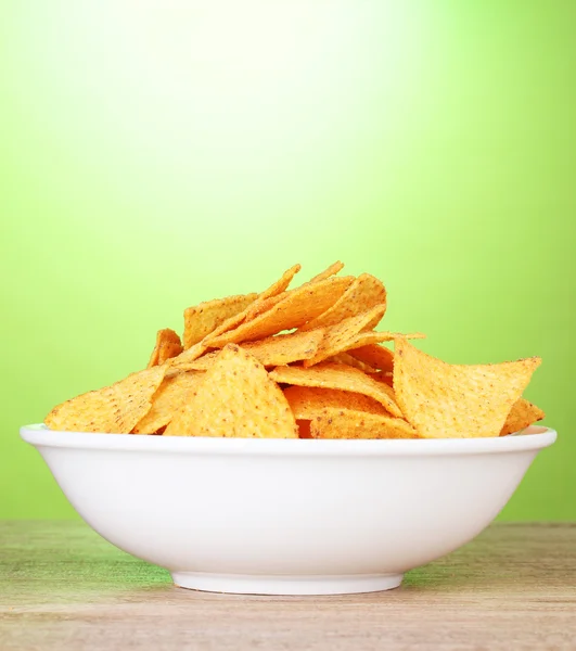 Tasty potato chips in white bowl on wooden table on green background — Stock Photo, Image