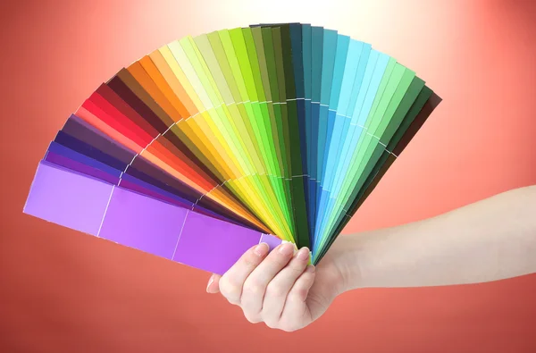 Hand som håller ljusa palett av färger på röd bakgrund — Stockfoto