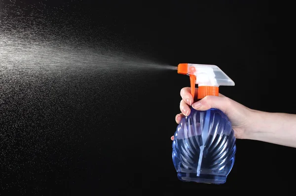 Mão segurando frasco de spray e pulverização em fundo preto — Fotografia de Stock
