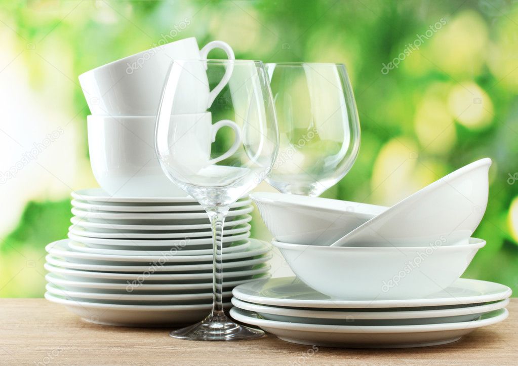 Clean dishes on wooden table on green background