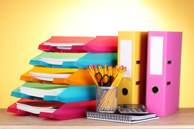 Bright paper trays and stationery on wooden table on yellow background clipart