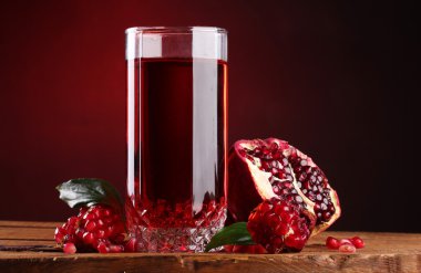 Ripe pomergranate and glass of juice on wooden table on red background clipart