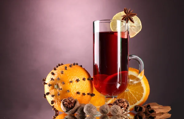 Mulled vin i glasset, krydderi og orange på lilla baggrund - Stock-foto