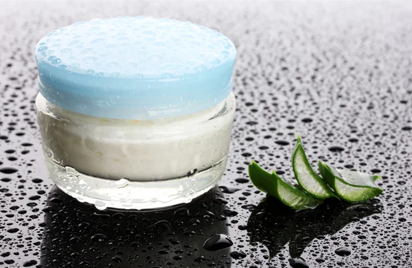 Closed glass jar of cream and aloe on black background with water droplets — Stock Photo, Image