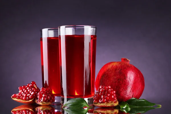 Ripe pomergranate and glasses of juice on purple background — Stock Photo, Image