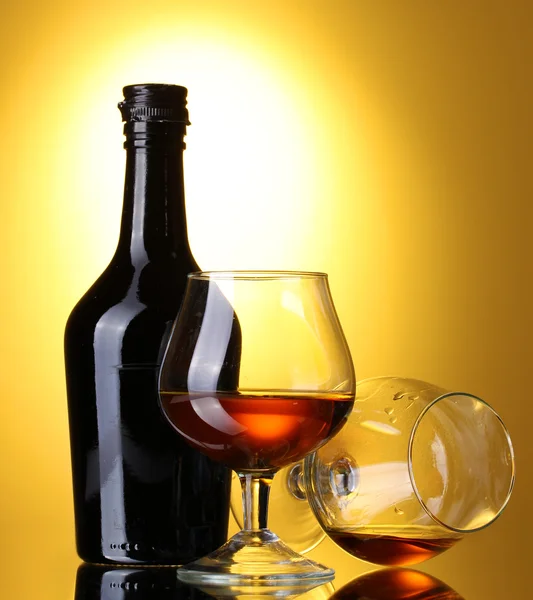Óculos de conhaque e garrafa sobre fundo amarelo — Fotografia de Stock