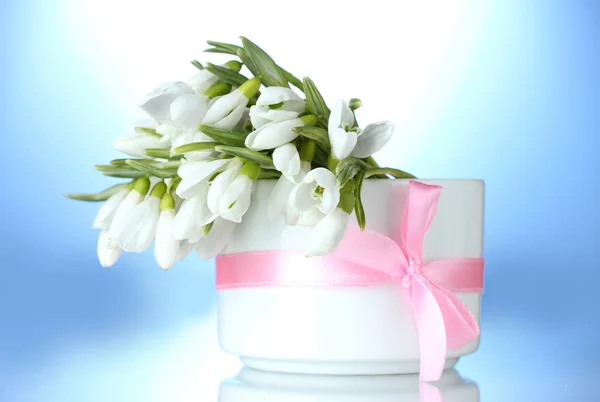 Beautiful bouquet of snowdrops in vase with bow on blue background — Stock Photo, Image