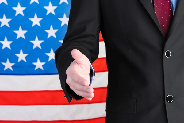 Empresario dando la mano por un apretón de manos en el fondo de la bandera estadounidense — Foto de Stock