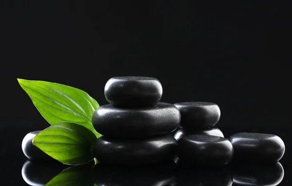 Wellness-Steine und grüne Blätter auf schwarzem Hintergrund — Stockfoto