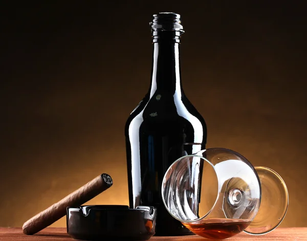 Botella y vaso de brandy y cigarro sobre mesa de madera sobre fondo marrón — Foto de Stock