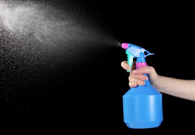 Hand holding spray bottle and spraying on black background clipart