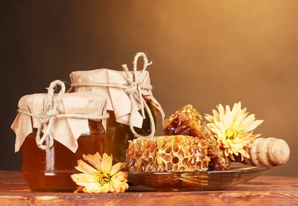 Twee potten van honing, honingraten en houten drizzler op tafel op gele achtergrond — Stockfoto