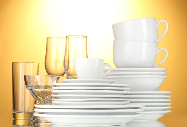 Üres tálak, tányérok, poharak és csészék a sárga háttér — Stock Fotó
