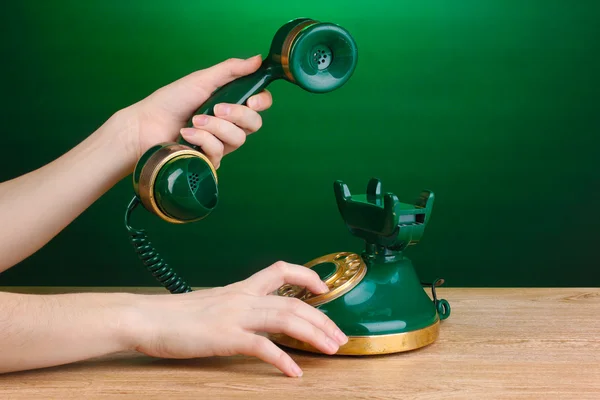 Dialing on retro phone on wooden table on green background — Stock Photo, Image