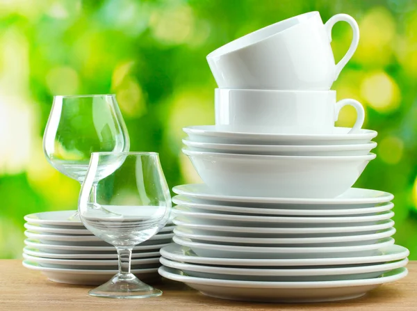 Clean dishes on wooden table on green background — Stock Photo, Image
