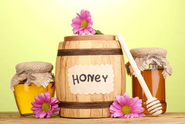 Miel dulce en barril y frascos con rociador sobre mesa de madera sobre fondo verde —  Fotos de Stock