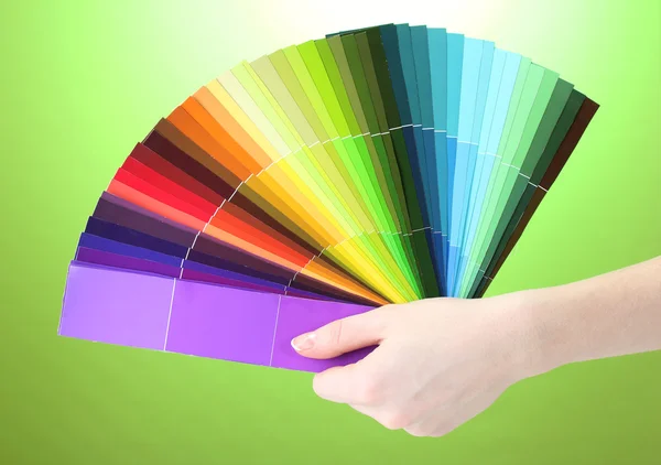 Mão segurando paleta brilhante de cores no fundo verde — Fotografia de Stock