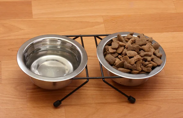Сухой корм для собак и вода в металлических мисках на полу — стоковое фото